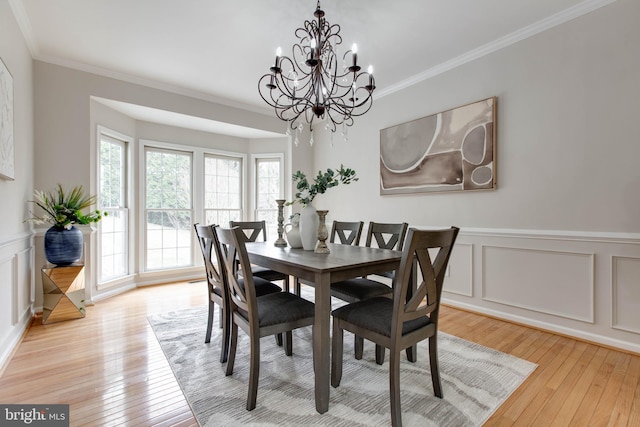 dining room with a decorative wall, wainscoting, light wood finished floors, and ornamental molding