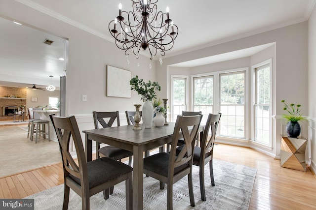 dining room with visible vents, baseboards, ornamental molding, light wood-style flooring, and a fireplace