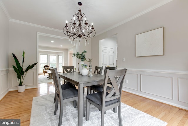 dining room with a decorative wall, light wood-style floors, a wainscoted wall, and ornamental molding