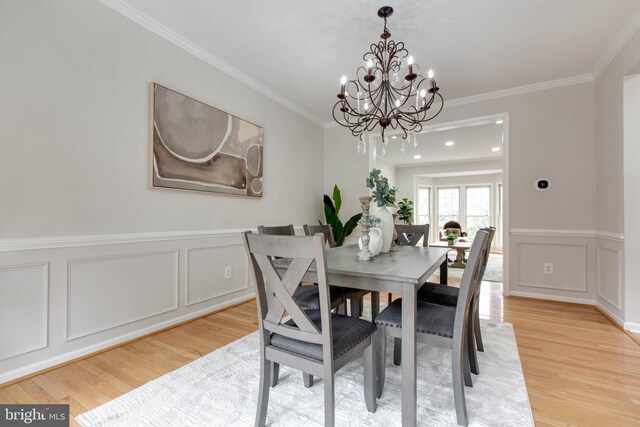 dining space featuring light wood-style floors, wainscoting, crown molding, and a decorative wall