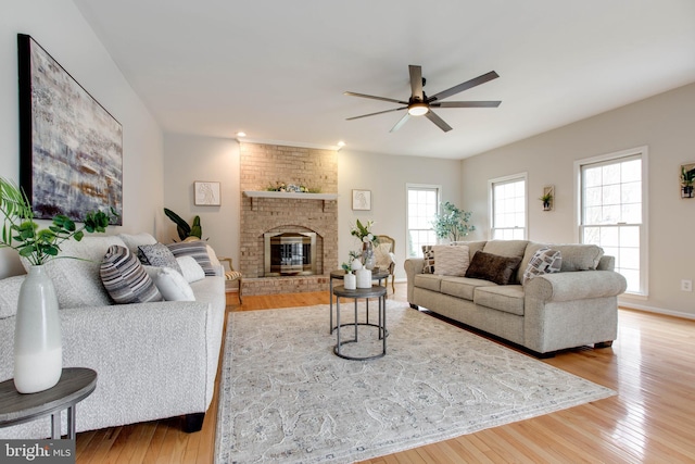 living area featuring light wood finished floors, a brick fireplace, and ceiling fan