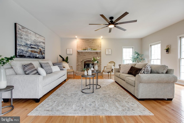 living room with a ceiling fan, a brick fireplace, and wood finished floors