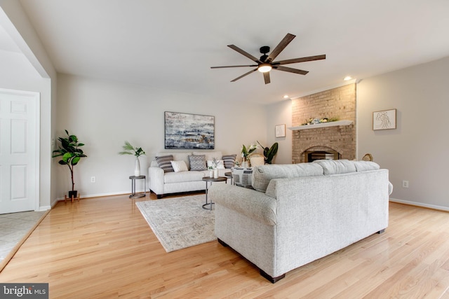 living area featuring recessed lighting, light wood-style floors, baseboards, a brick fireplace, and ceiling fan