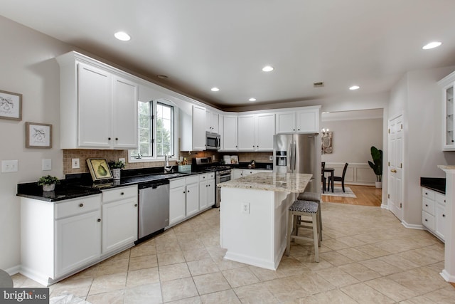 kitchen with a sink, decorative backsplash, stainless steel appliances, white cabinets, and a kitchen bar