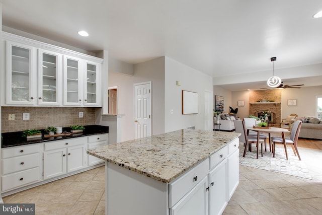 kitchen featuring backsplash, open floor plan, white cabinets, light stone countertops, and a brick fireplace