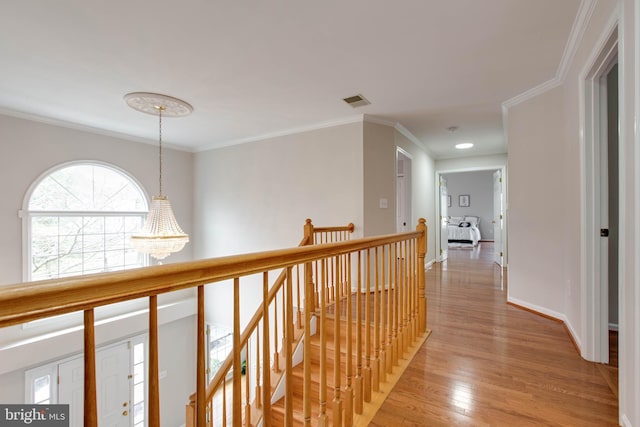 corridor with visible vents, crown molding, an upstairs landing, an inviting chandelier, and light wood-style floors