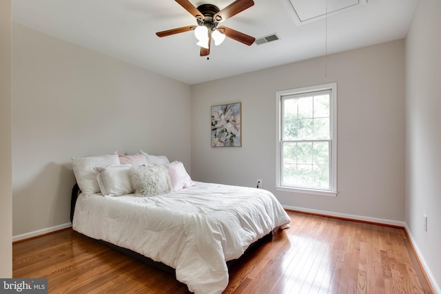 bedroom with visible vents, baseboards, attic access, and wood finished floors