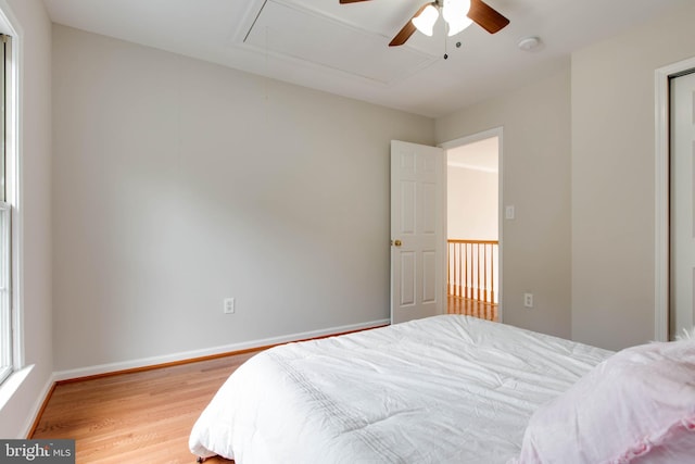 bedroom with baseboards, attic access, light wood-style flooring, and a ceiling fan