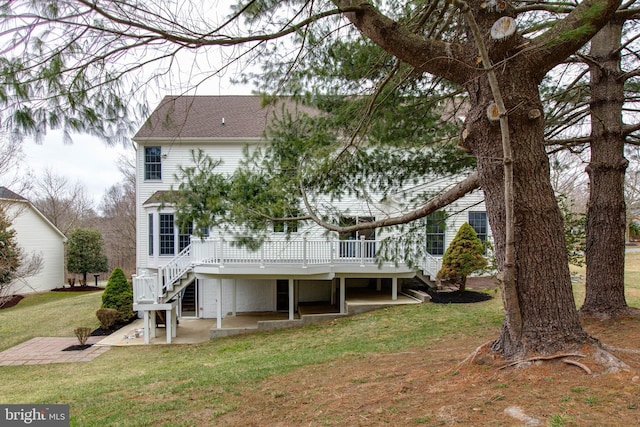 back of property featuring a lawn, a deck, a shingled roof, stairs, and a patio area