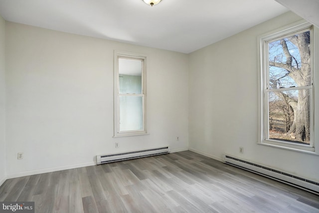 unfurnished room with baseboard heating, light wood-type flooring, and baseboards