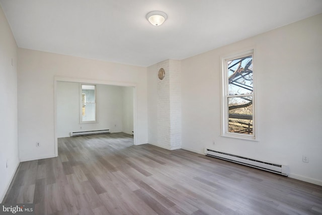 empty room featuring light wood-style floors, plenty of natural light, and a baseboard heating unit