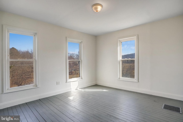 empty room featuring wood finished floors, visible vents, and baseboards