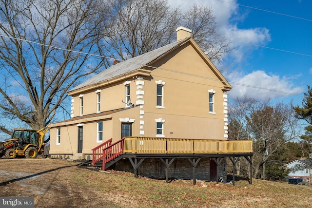 rear view of property with stucco siding, a chimney, and a wooden deck