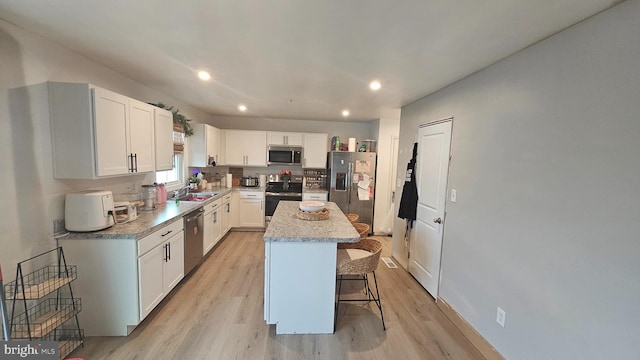 kitchen with a breakfast bar area, stainless steel appliances, white cabinets, a kitchen island, and sink