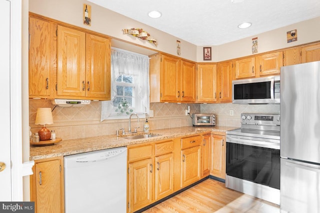 kitchen with appliances with stainless steel finishes, tasteful backsplash, sink, light stone countertops, and light wood-type flooring