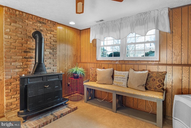 living area featuring carpet, wood walls, ceiling fan, and a wood stove