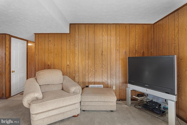 sitting room featuring light colored carpet, wooden walls, and a textured ceiling