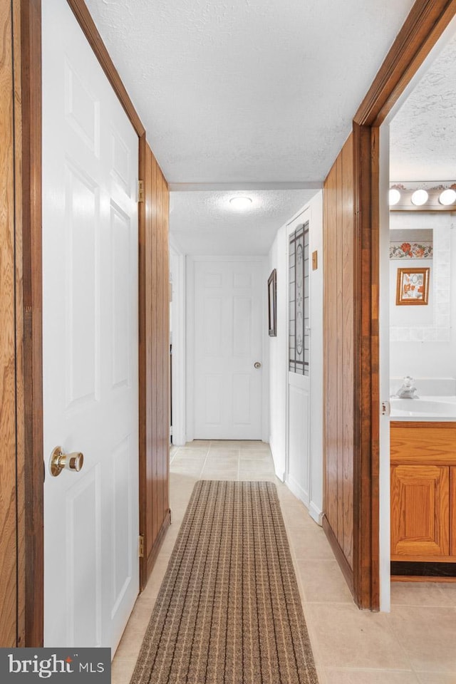 corridor with sink, a textured ceiling, and light tile patterned flooring