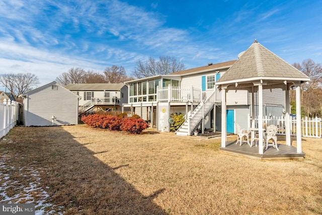 back of house featuring a wooden deck, a sunroom, and a lawn