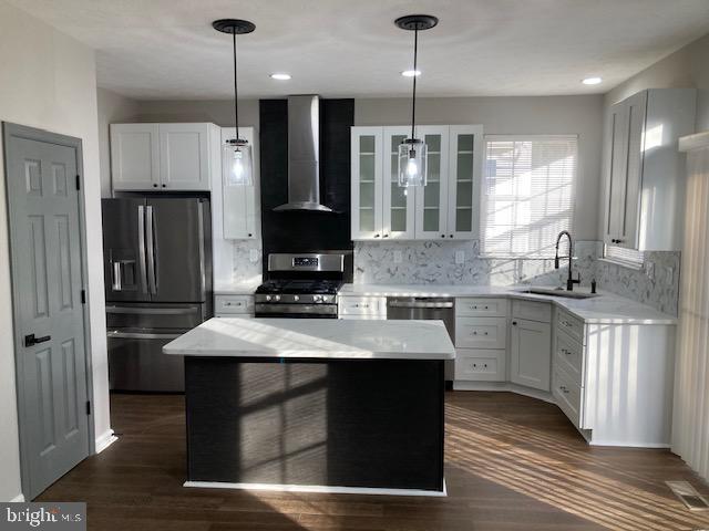 kitchen featuring a center island, stainless steel appliances, glass insert cabinets, white cabinets, and wall chimney range hood