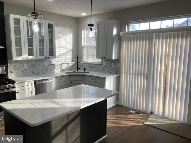 kitchen with hanging light fixtures, appliances with stainless steel finishes, glass insert cabinets, and a sink