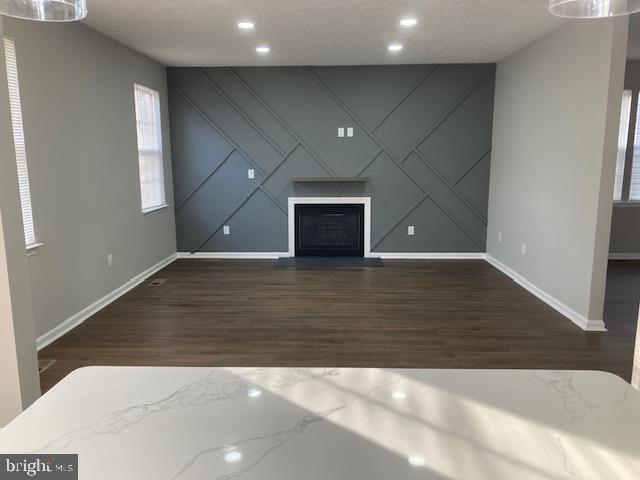 unfurnished living room with a fireplace, baseboards, dark wood-type flooring, and recessed lighting