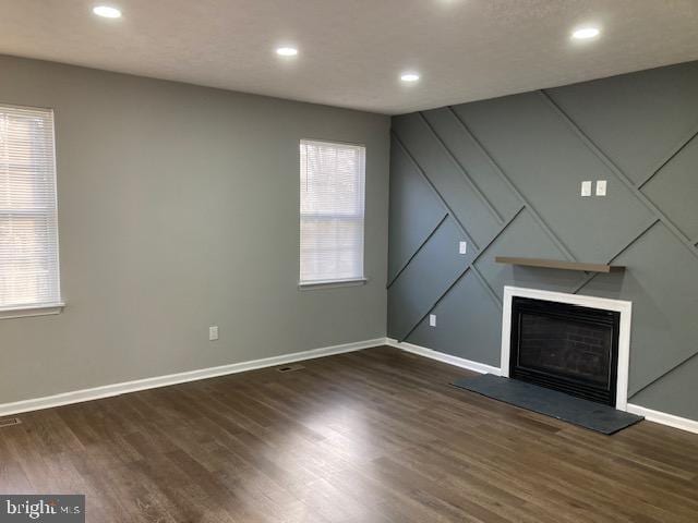 unfurnished living room with a fireplace with raised hearth, dark wood-type flooring, recessed lighting, and baseboards