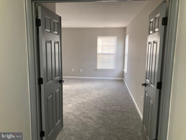 empty room featuring baseboards, dark carpet, and a textured ceiling