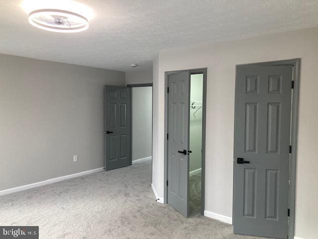 unfurnished bedroom with a textured ceiling, a closet, baseboards, and light colored carpet