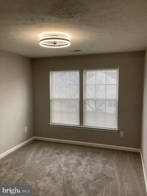 spare room featuring carpet floors, baseboards, and a textured ceiling