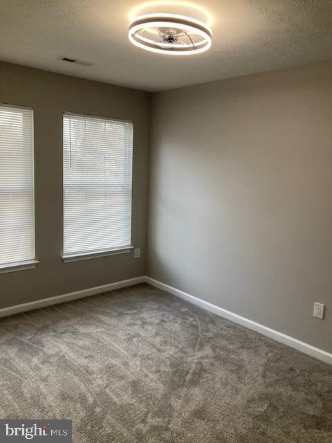 empty room featuring a textured ceiling, carpet floors, and visible vents