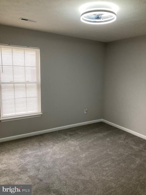 empty room featuring dark colored carpet, visible vents, and baseboards