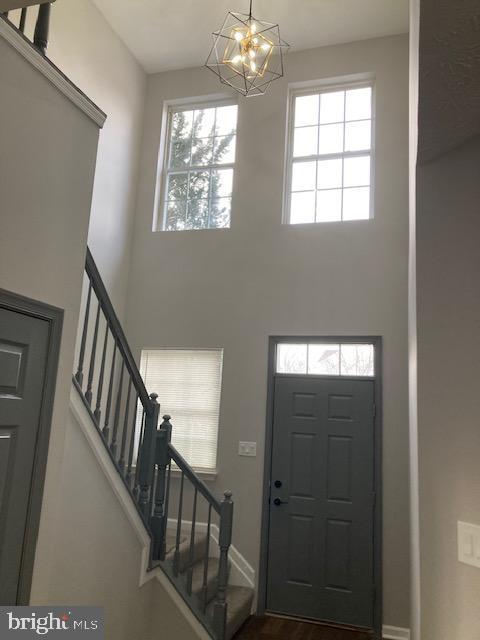 foyer featuring stairs, a towering ceiling, a wealth of natural light, and a chandelier