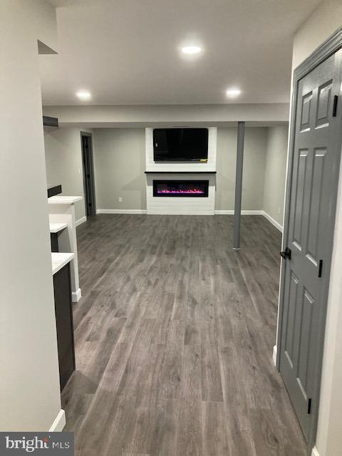 finished below grade area featuring a lit fireplace, dark wood-type flooring, and baseboards