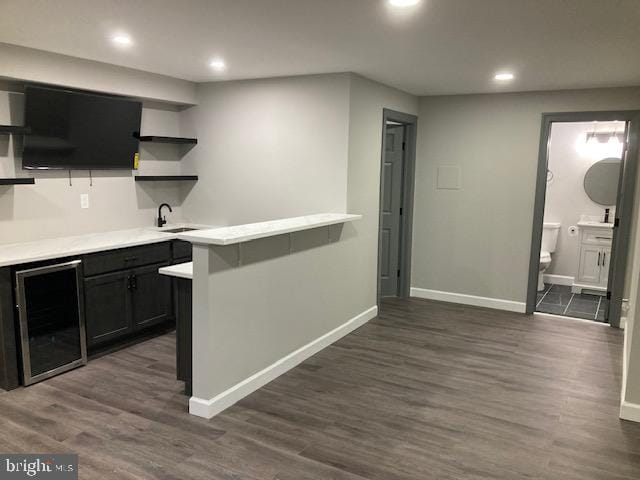 bar with a sink, beverage cooler, baseboards, and dark wood-style flooring