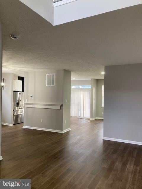 empty room featuring dark wood-type flooring, visible vents, a textured ceiling, and baseboards