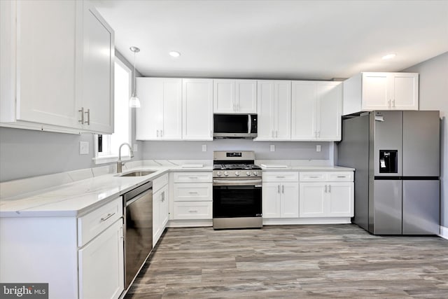 kitchen featuring sink, appliances with stainless steel finishes, white cabinetry, light stone counters, and light wood-type flooring