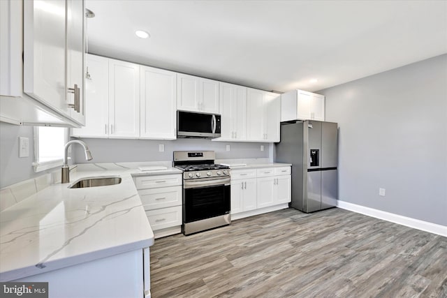 kitchen featuring appliances with stainless steel finishes, sink, white cabinets, light stone countertops, and light hardwood / wood-style flooring