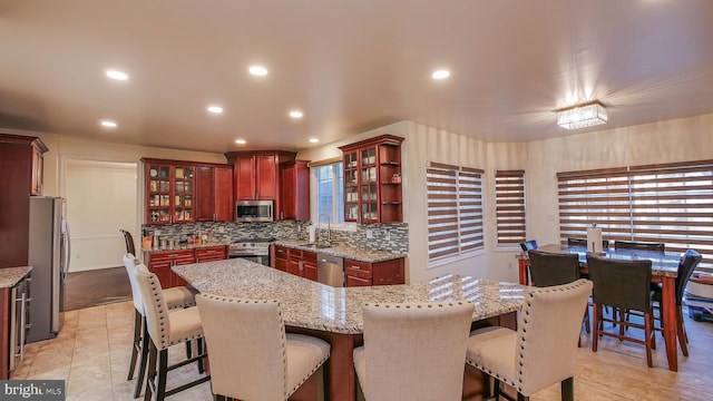 kitchen with tasteful backsplash, sink, a center island, stainless steel appliances, and light stone countertops