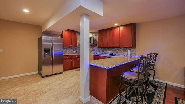 kitchen with tasteful backsplash, a breakfast bar area, light stone counters, kitchen peninsula, and stainless steel refrigerator with ice dispenser