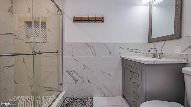 bathroom with tile walls, an enclosed shower, vanity, and toilet