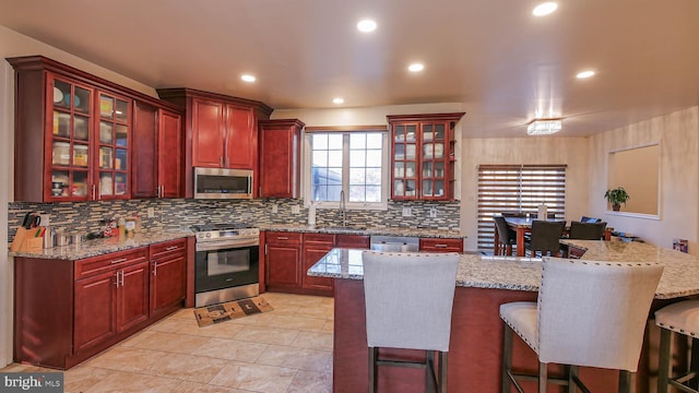 kitchen with light stone counters, sink, backsplash, and stainless steel appliances