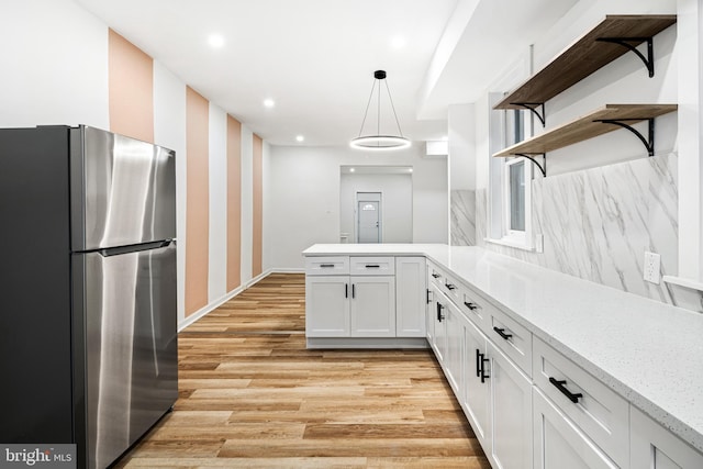 kitchen featuring stainless steel refrigerator, white cabinetry, decorative light fixtures, kitchen peninsula, and light wood-type flooring