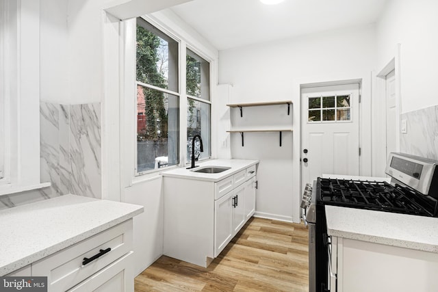 kitchen featuring white cabinetry, sink, light hardwood / wood-style floors, gas range, and light stone countertops