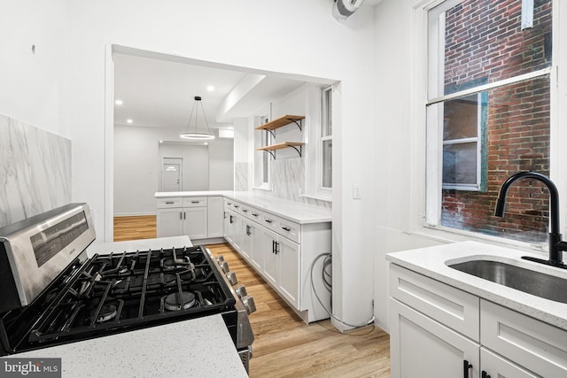 kitchen featuring pendant lighting, sink, white cabinetry, light stone countertops, and gas stove