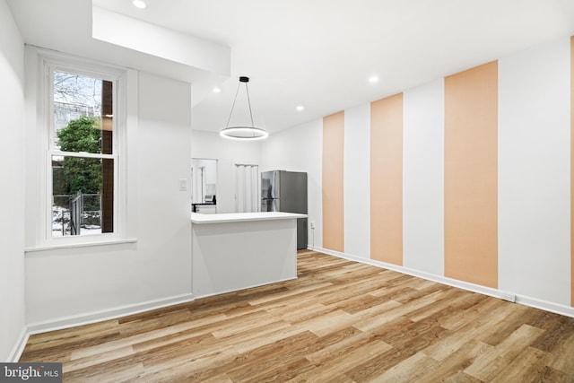 kitchen featuring hanging light fixtures, stainless steel fridge, light wood-type flooring, and kitchen peninsula