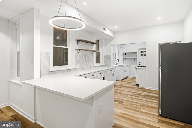 kitchen with sink, white cabinetry, hanging light fixtures, stainless steel refrigerator, and kitchen peninsula