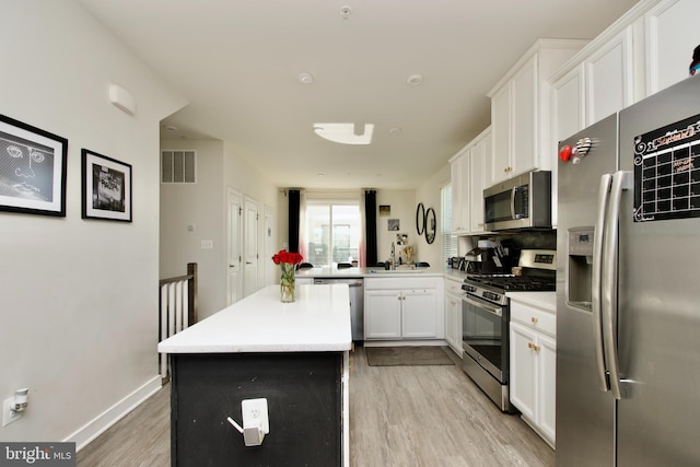 kitchen with light hardwood / wood-style flooring, stainless steel appliances, white cabinets, a kitchen island, and kitchen peninsula