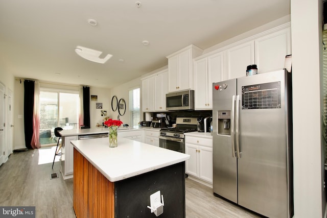 kitchen featuring stainless steel appliances, kitchen peninsula, a kitchen island, and white cabinets