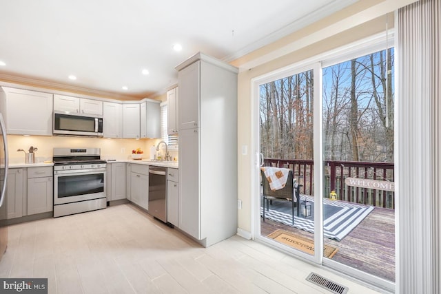 kitchen featuring visible vents, appliances with stainless steel finishes, ornamental molding, light countertops, and a sink